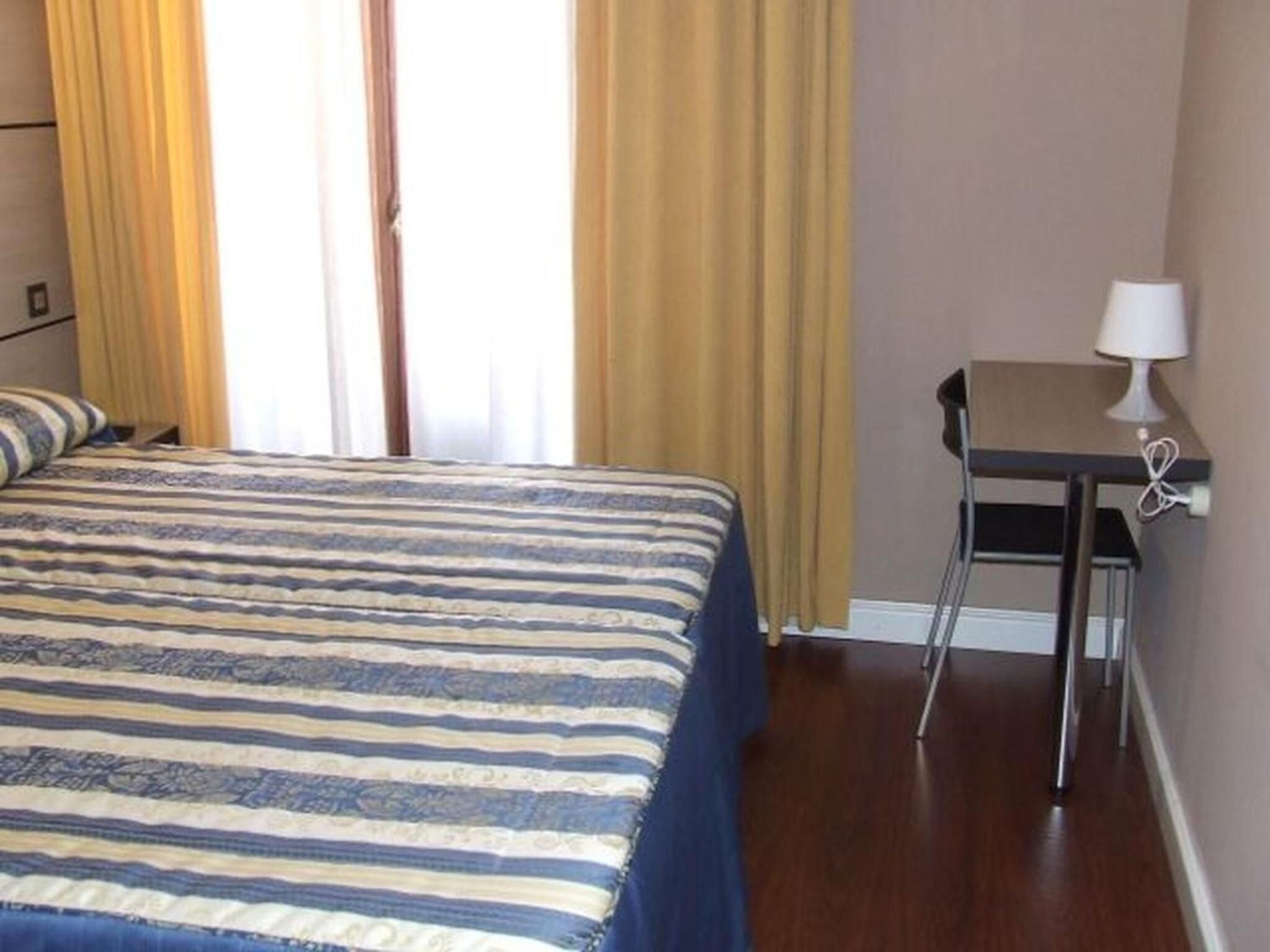 Una habitación de hotel con cama, escritorio y lámpara.