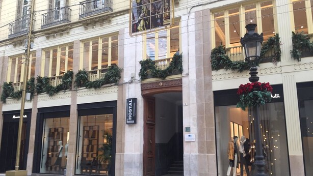 A hotel facade with a large entrance, a sign for 'Hostal', and a staircase leading to the entrance. - Hostal Larios (Málaga)