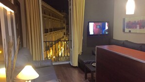 A modern living room with a leather sofa, a small table, a TV, and a balcony with a railing. - Hostal Larios (Málaga)