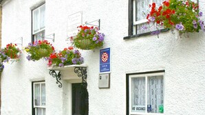 A white building with hanging flower baskets and a sign indicating no vacancies. - Willance House Guest House (Richmond)