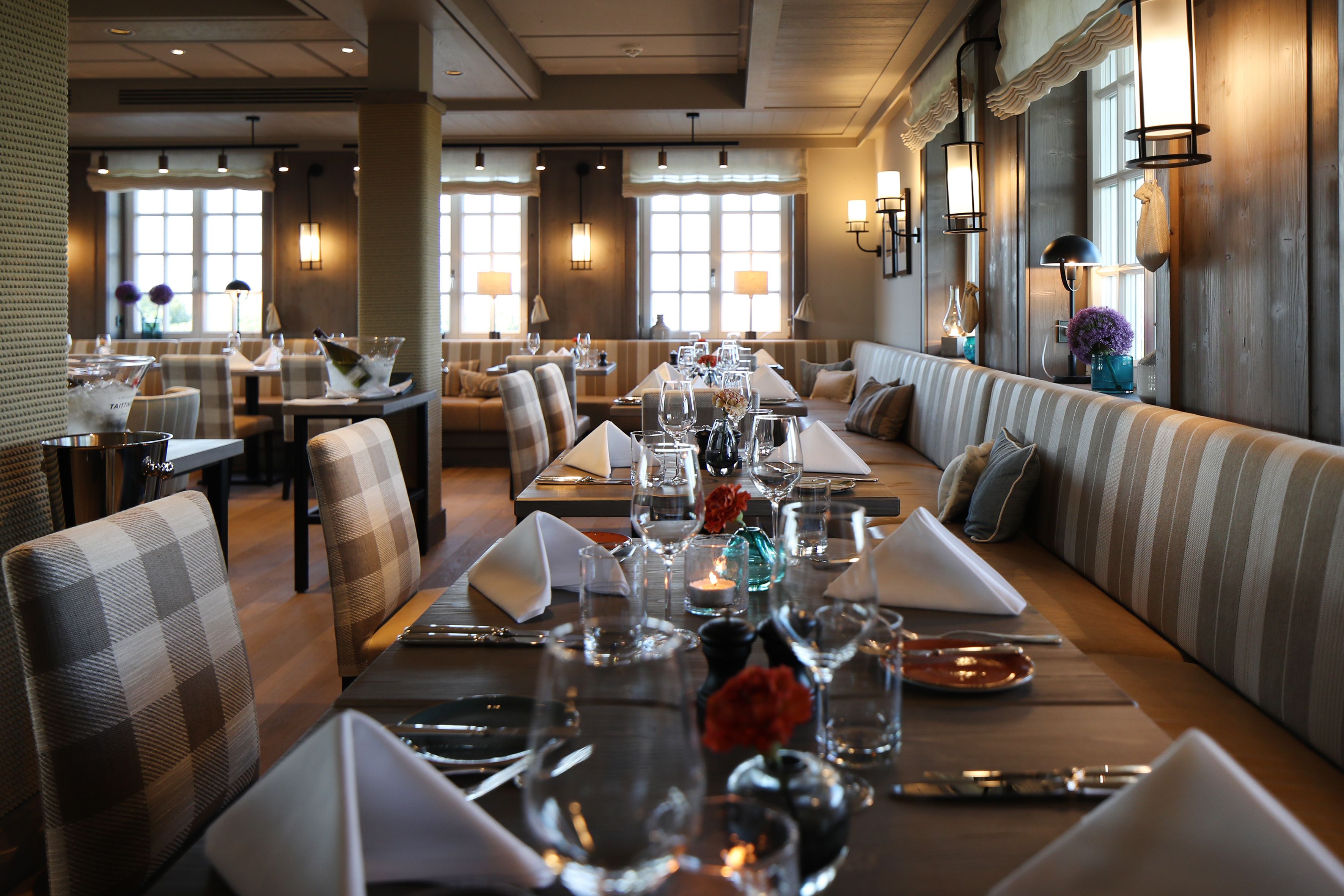 Un restaurante con mesas largas dispuestas para comer, asientos acolchados e iluminación ambiental.