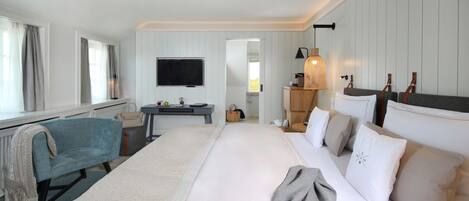 A hotel room with a large bed, a sofa, a television, and a desk with a lamp.