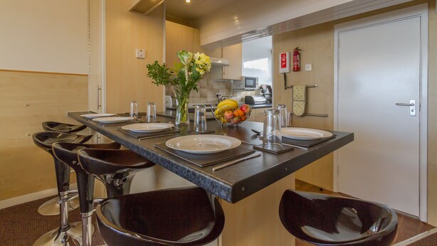 A modern kitchen with a central island, bar stools, and a fruit bowl. - Lynton Apartments (Blackpool)