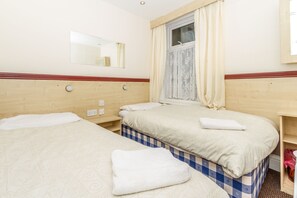 Habitación de hotel con dos camas, una ventana con cortinas, un espejo y cabecera de madera.