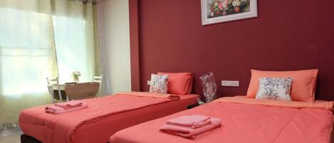 Una habitación con dos camas, cada una con ropa de cama rosa y almohadas decorativas. Hay un cuadro enmarcado en la pared sobre las camas.