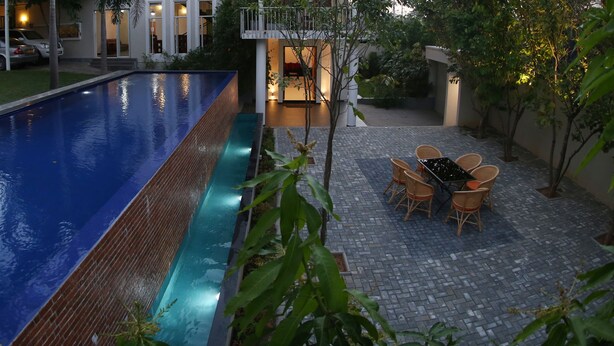 A swimming pool with a tiled deck and a dining area with wicker chairs. - Capital Villa (Battaramulla)
