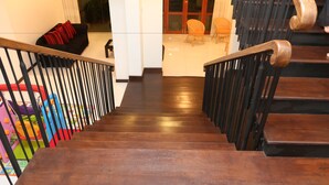 A wooden staircase with black railings leading to a living area with a sofa and chairs. - Capital Villa (Battaramulla)