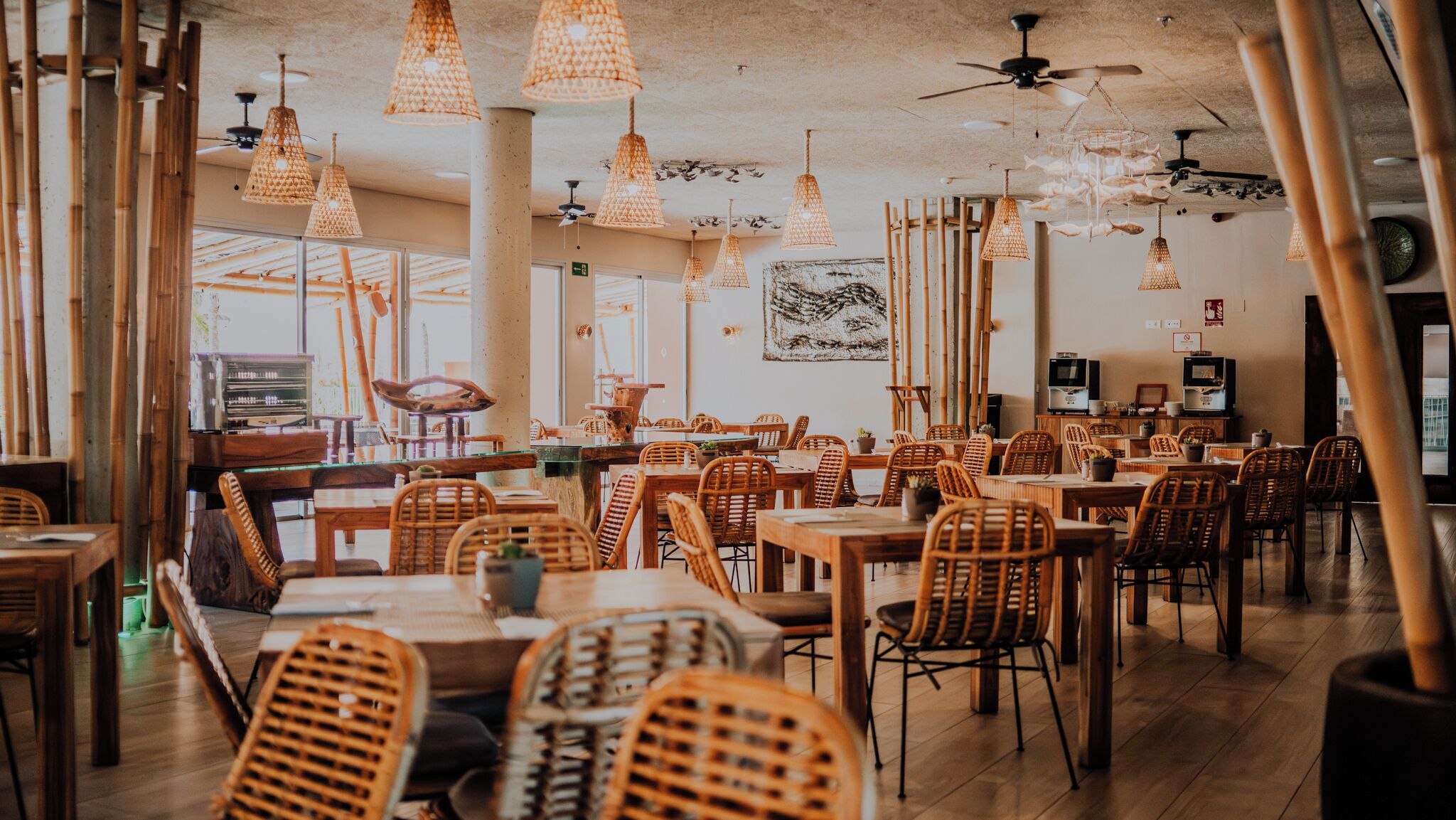 Un restaurante con columnas de bambú, muebles de mimbre e iluminación colgante.