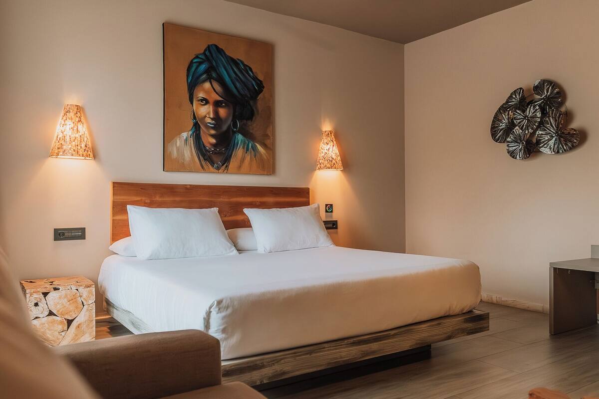 Una habitación de hotel con una cama, dos lámparas de pared, un cuadro y un adorno mural.