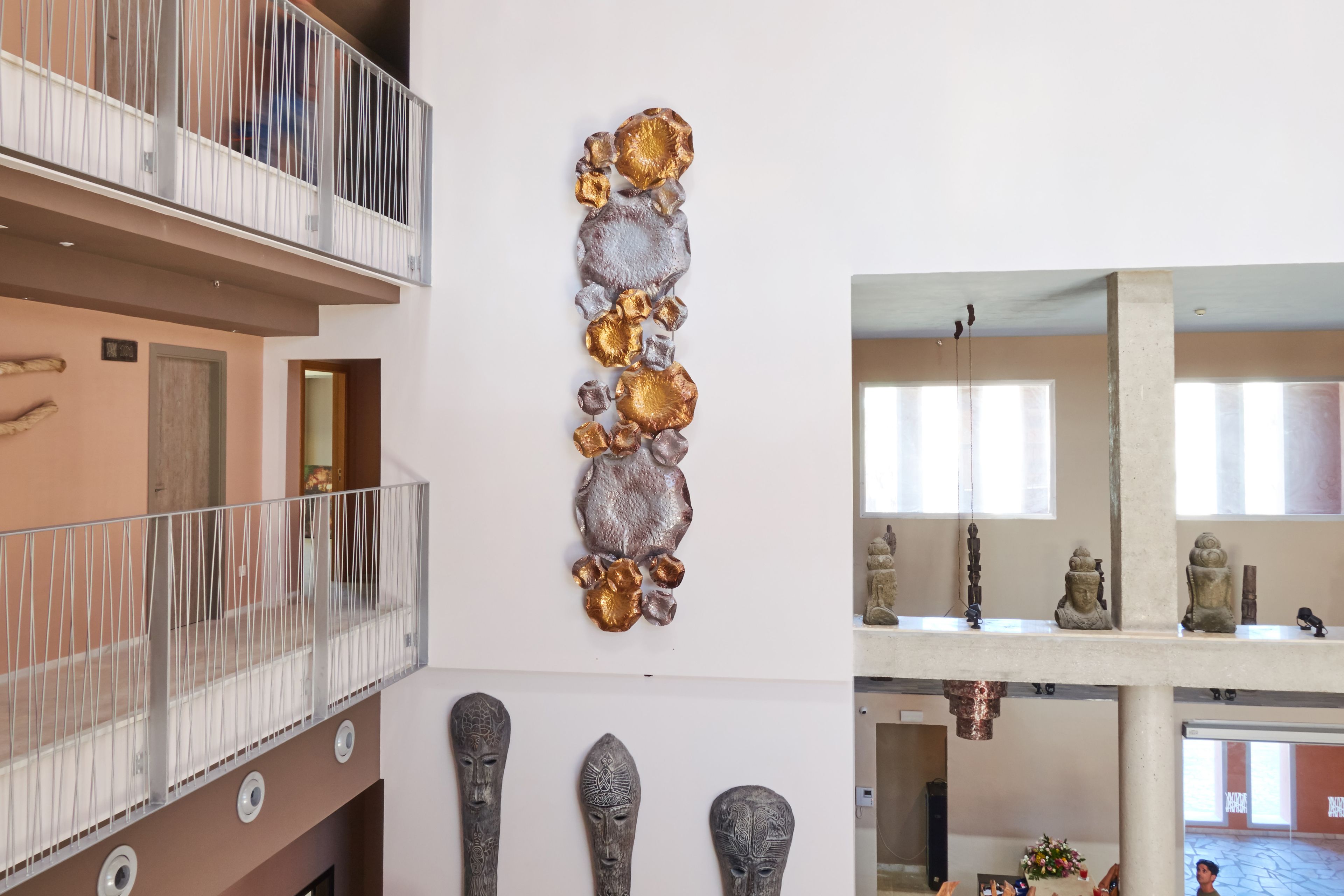 A multi-level interior with a balcony, a wall-mounted sculpture, and a series of statues.