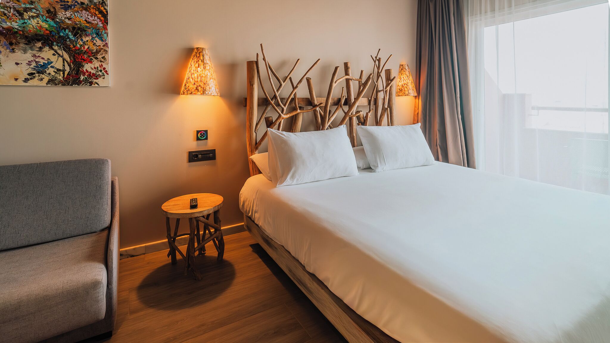A hotel room with a bed, a chair, a small table, and wall-mounted lamps.