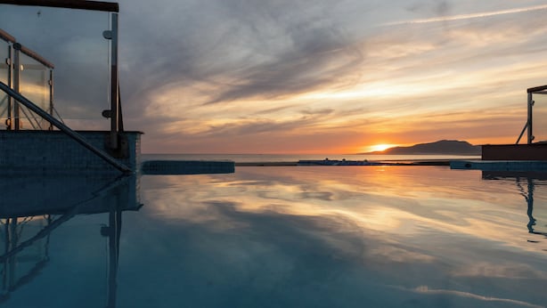 Piscina con vista al atardecer, cielo despejado y tierra distante.