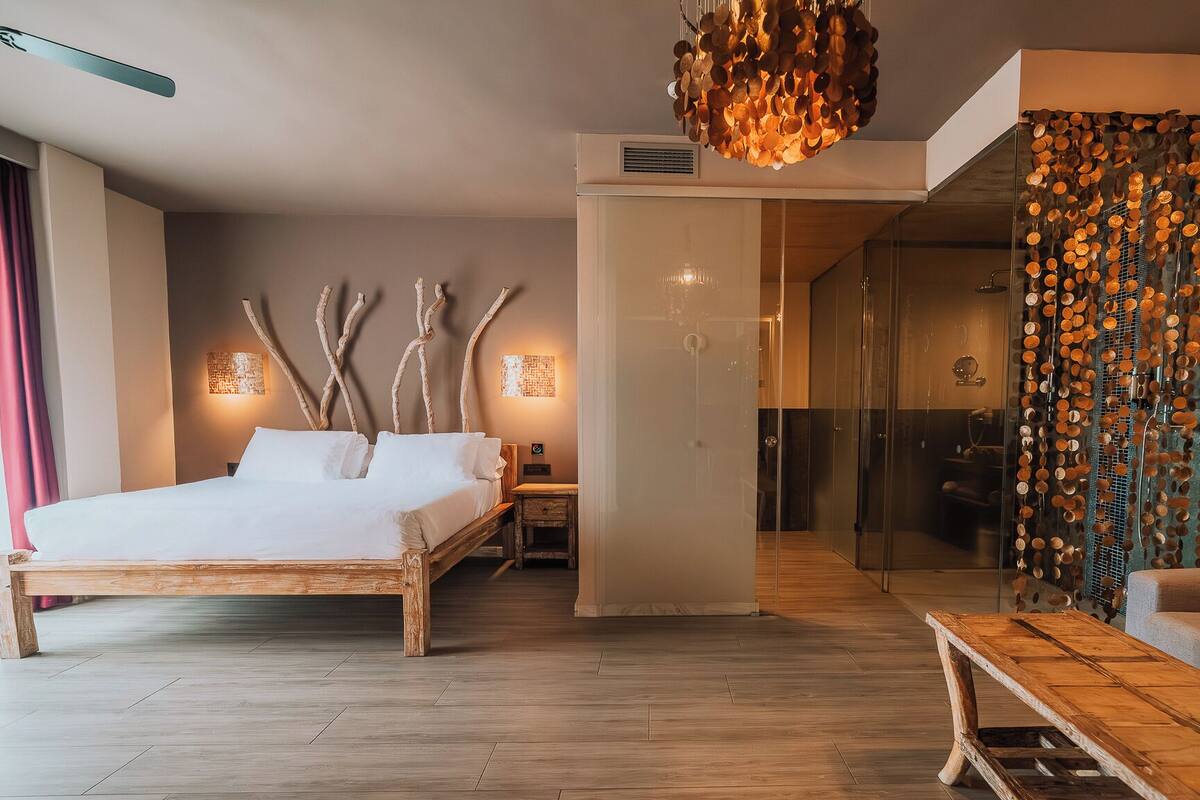 Una habitación de hotel moderna con una cama de madera, ducha de vidrio y una decoración de pared original.