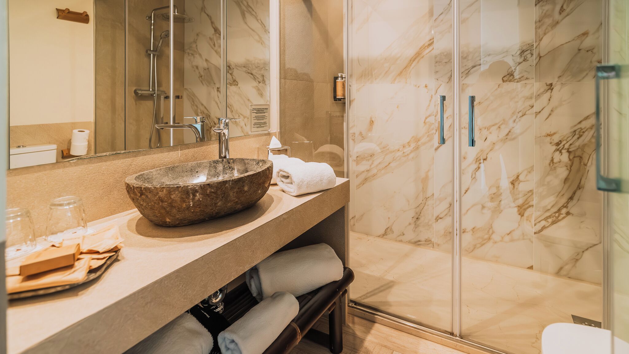Un baño con lavabo de piedra, espejo, toallero y cabina de ducha de vidrio.