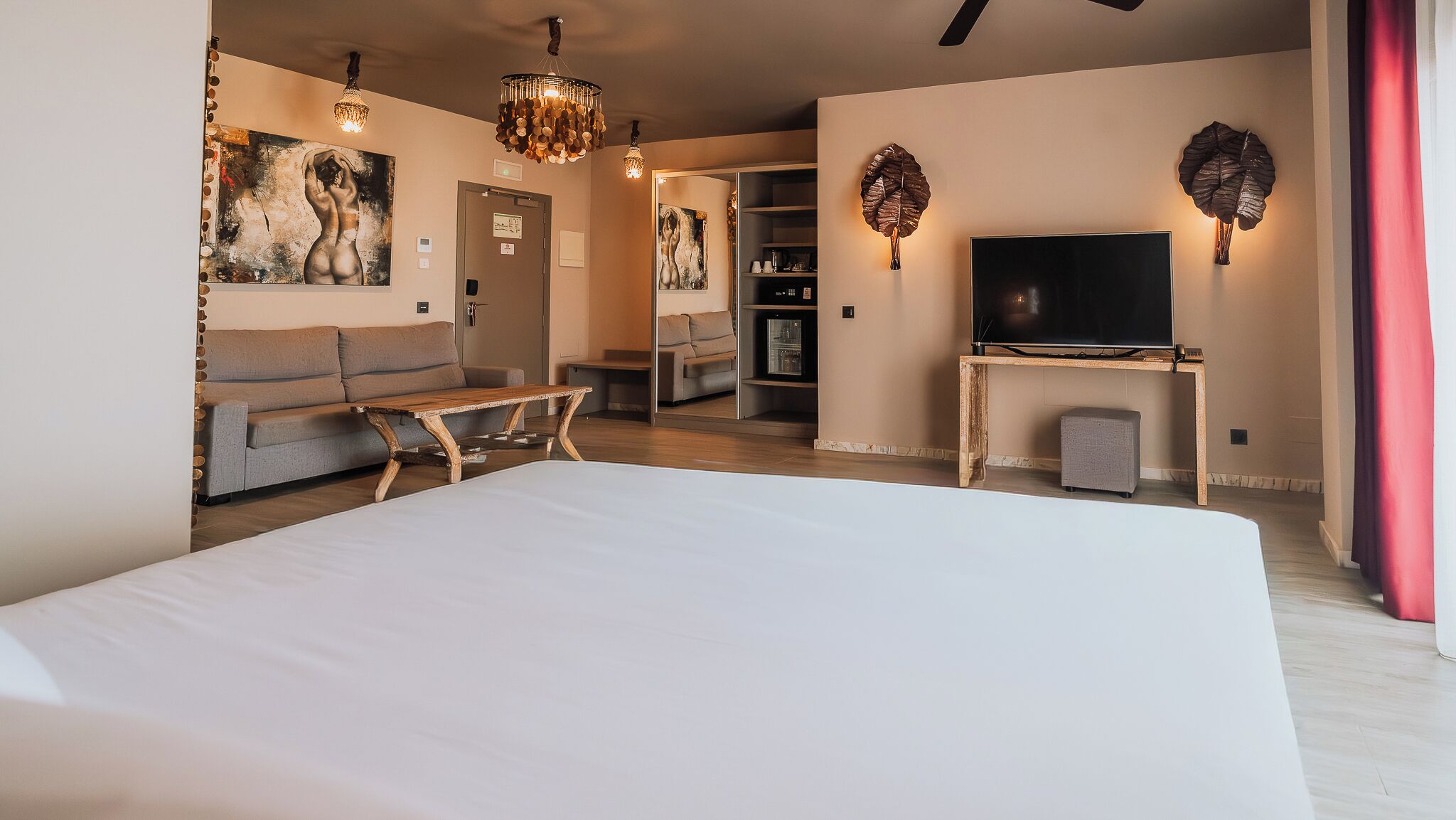 A modern hotel room with a large bed, a sofa, a TV, and a fireplace.