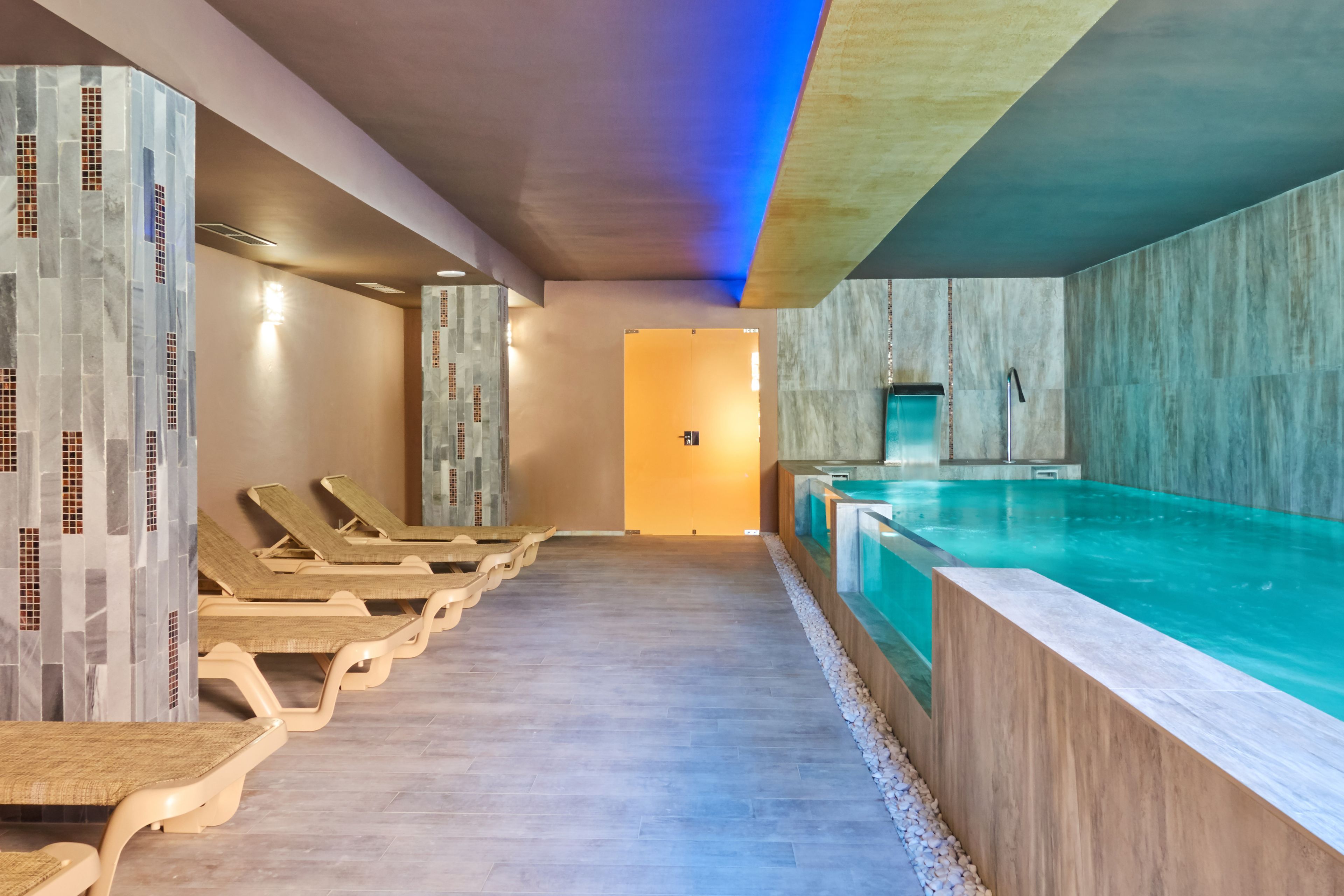 Un área de piscina interior moderna con sillones de descanso y una mesa de recepción.