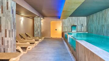 Un área de piscina interior moderna con sillones de descanso y una mesa de recepción.
