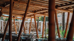 Un espacio de estar al aire libre cubierto con postes de bambú, paredes de piedra y mobiliario exterior.