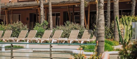 A pool area with lounge chairs, palm trees, and a building with balconies in the background.