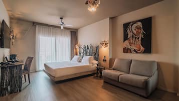 Una habitación de hotel moderna con cama, sofá, escritorio con computadora y un cuadro grande en la pared.