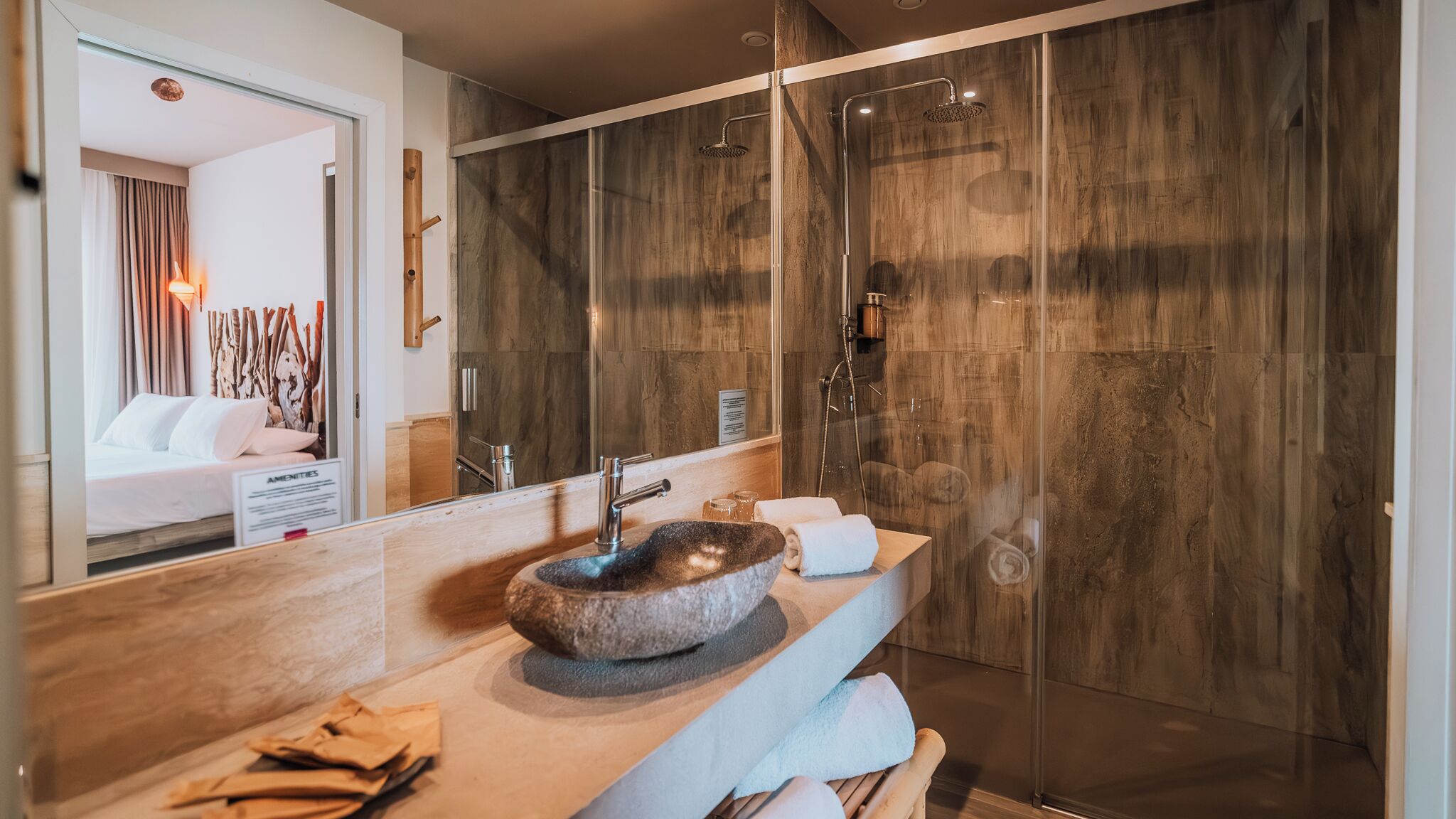 A modern bathroom with a stone sink, a glass shower enclosure, and a large mirror.