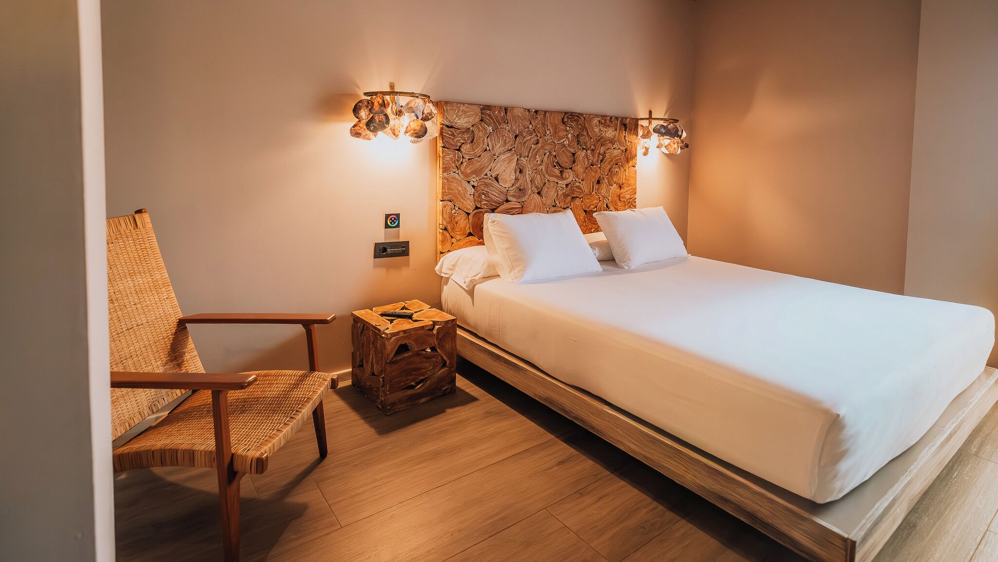 Habitación de hotel con cama, una silla, una mesita y una lámpara fijada en la pared.