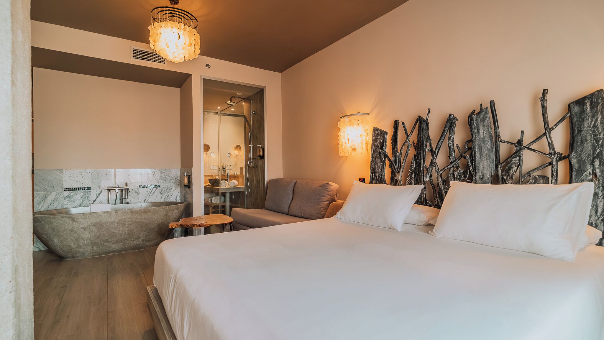 Un dormitorio con una cama grande, una bañera, una mesa de madera y una lámpara fijada a la pared.