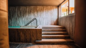 Una escalera de madera que lleva a una bañera con un grifo de metal, frente a una pared con textura.