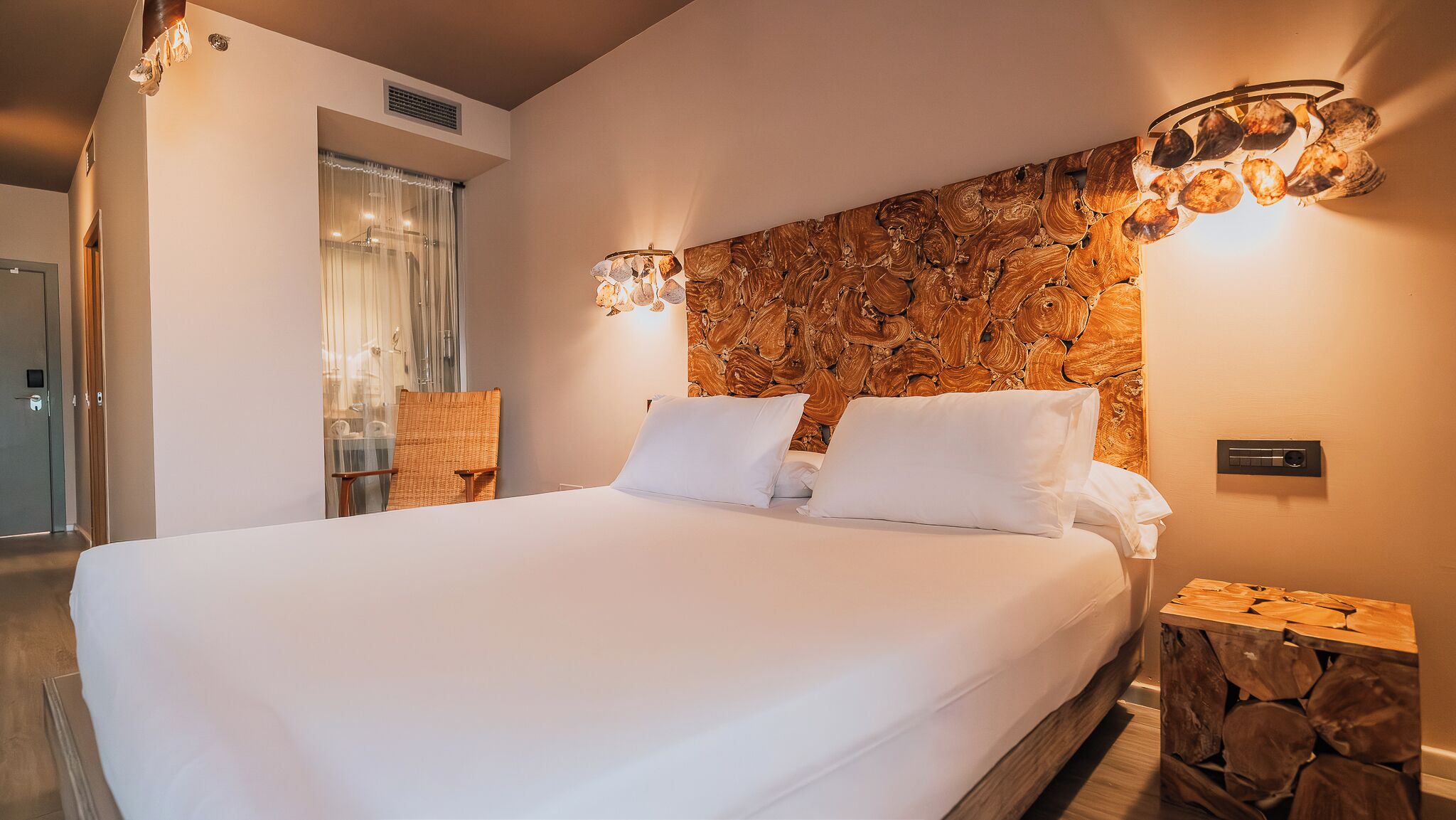 A hotel room with a large bed, a wooden headboard, a nightstand, and a window with curtains.