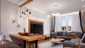 Una sala de estar moderna con una mesa de comedor de madera, un sofá, un televisor y un amplio ventanal con cortinas.