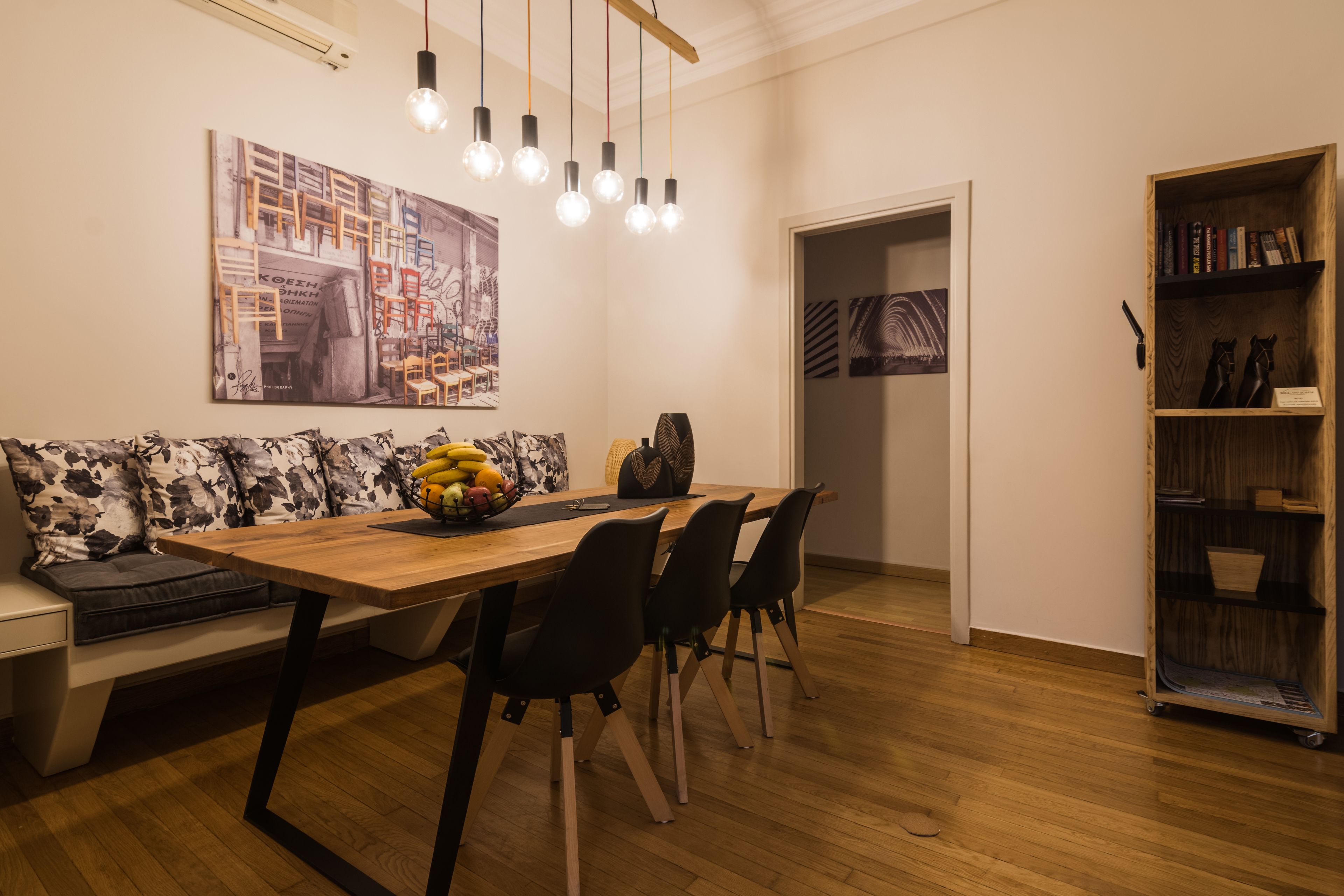 Un comedor con una mesa de madera, sillas negras, un sofá floral y una estantería.