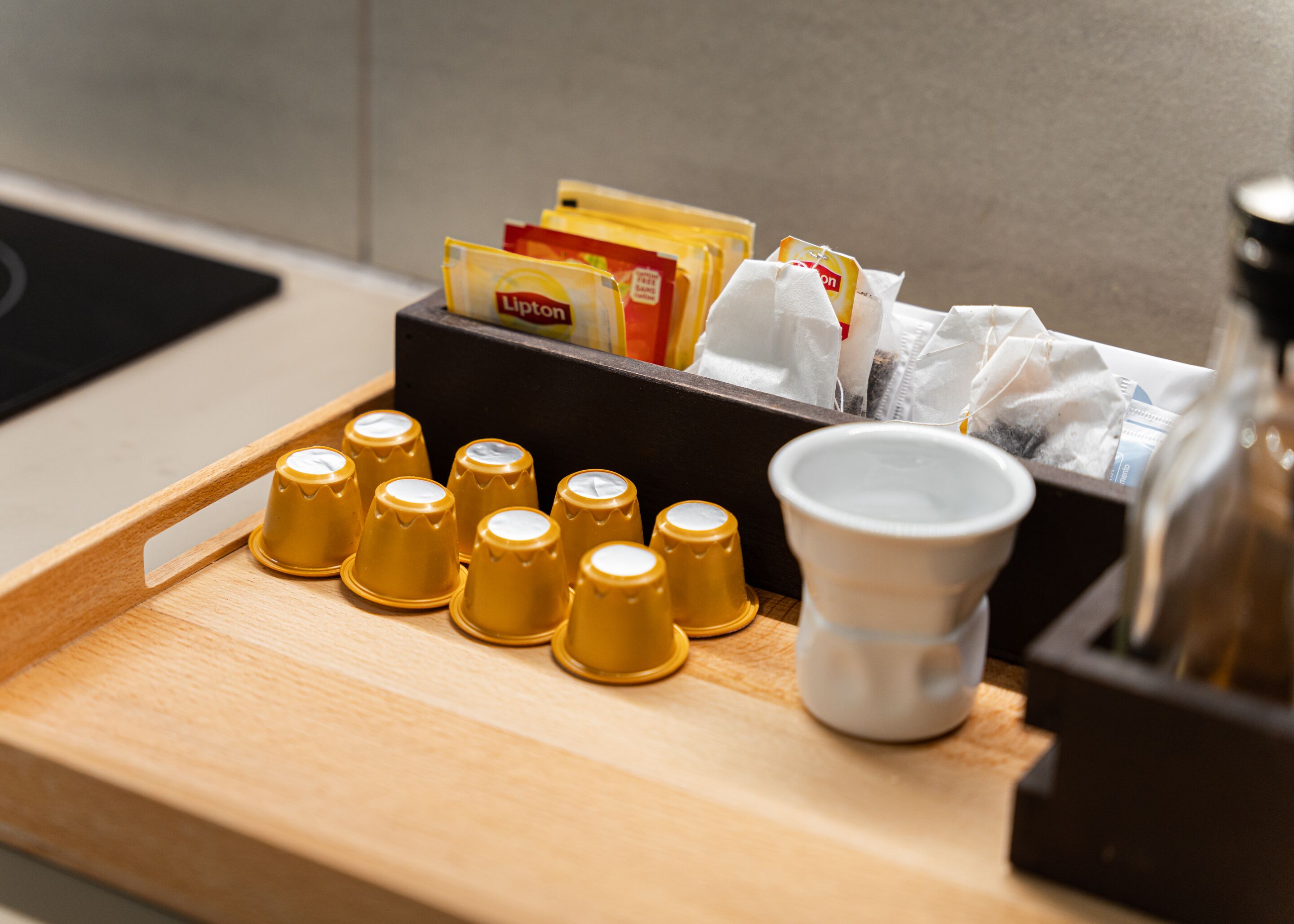 A tray with coffee cups, Lipton tea bags, and a white cup on a wooden surface.