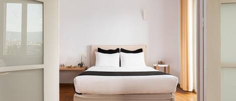 A neatly arranged bedroom with a large bed, a bedside table, a nightstand, and a view through a window.