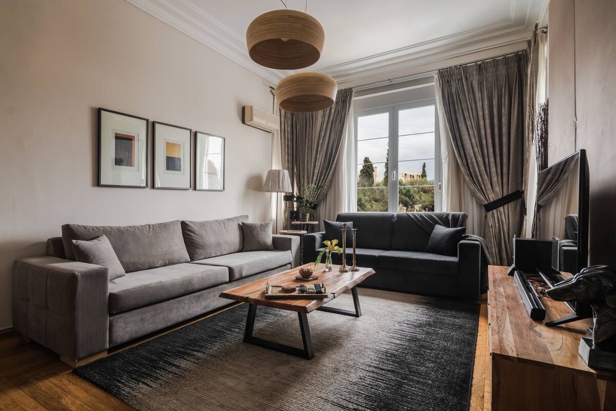 A modern living room with a grey sofa, a wooden coffee table, and a TV on a wooden stand.