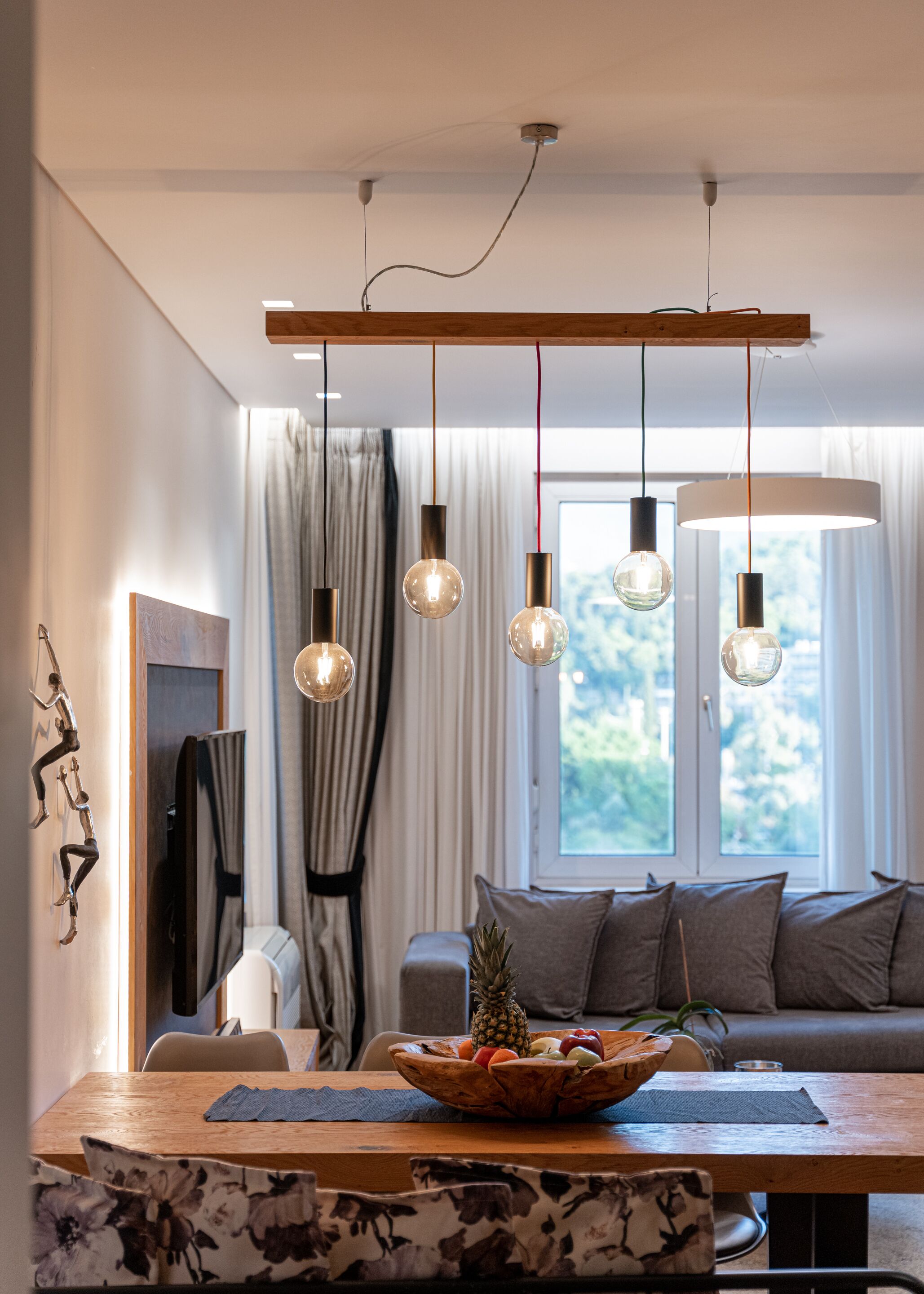 Un salón moderno con una mesa de comedor de madera, un frutero, un sofá e iluminación colgante.