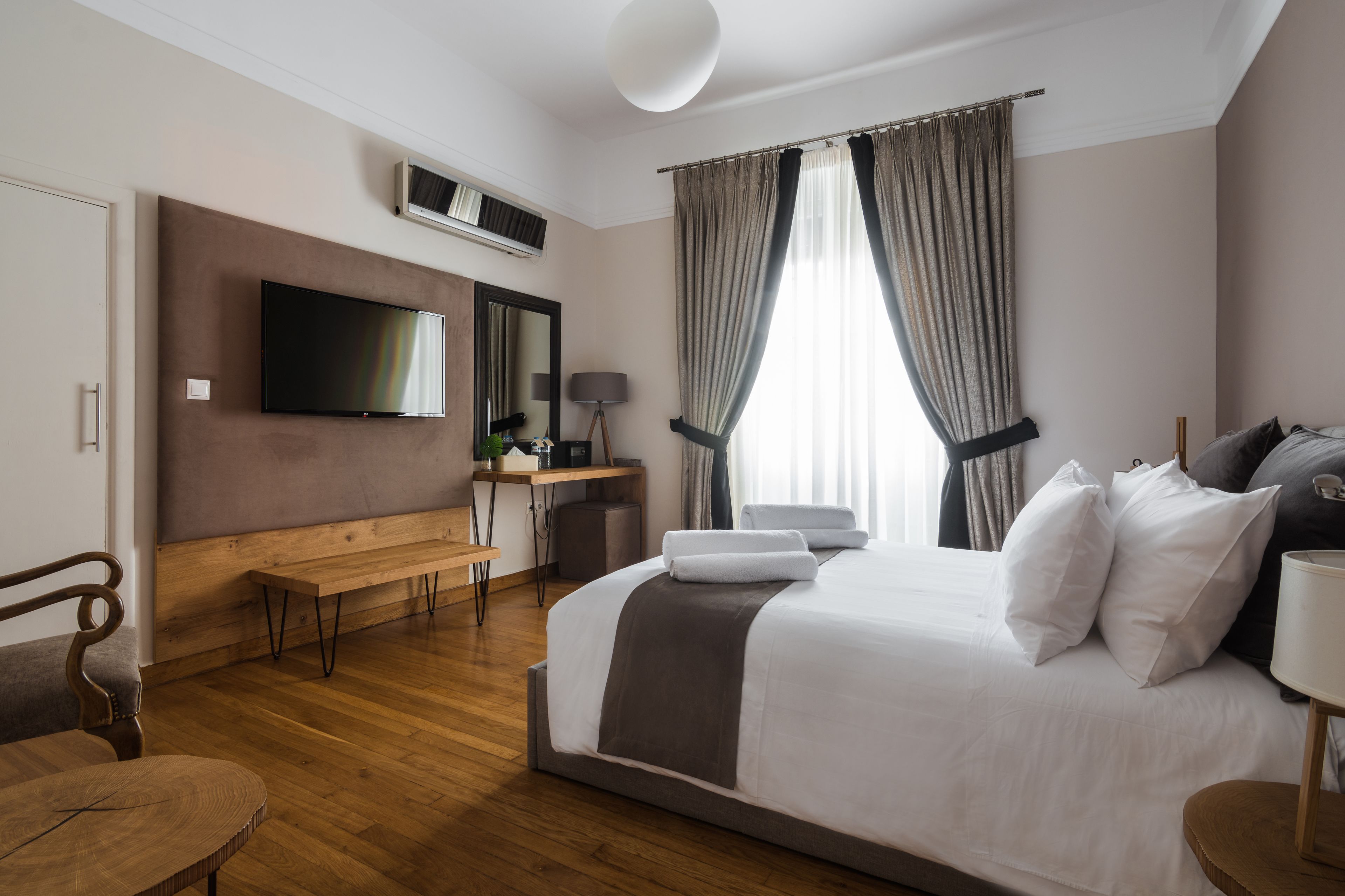 Une chambre d’hôtel avec un grand lit, un bureau avec un ordinateur, un téléviseur fixé au mur et une fenêtre avec des rideaux.