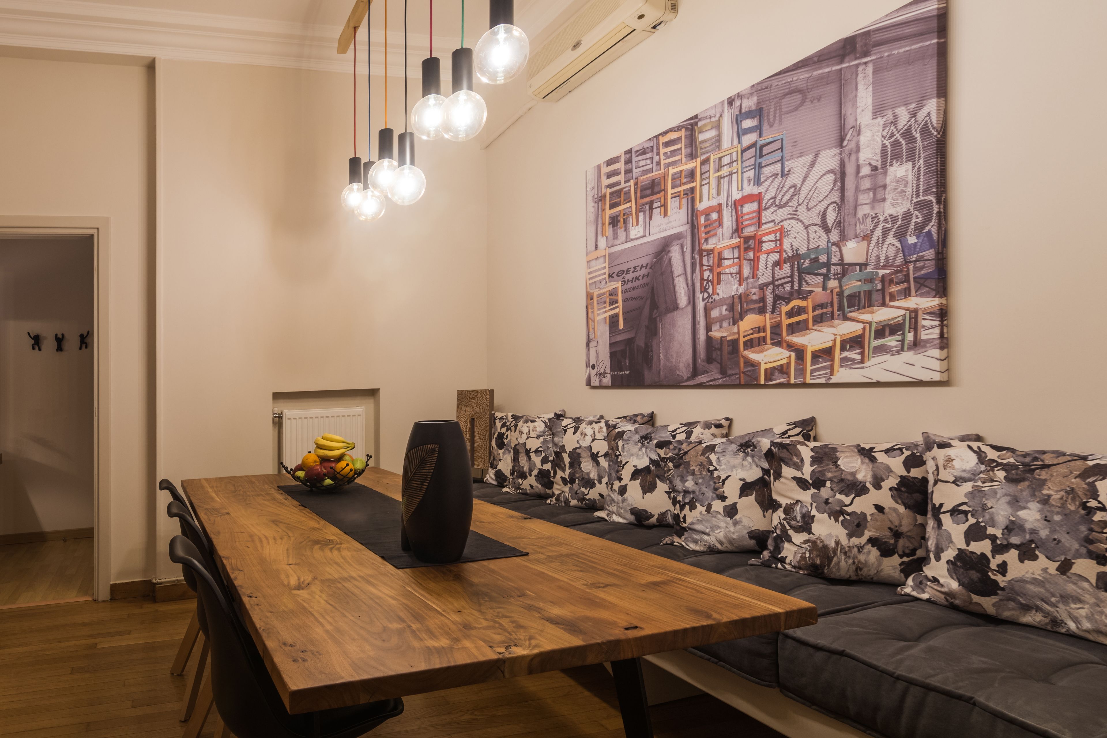 Comedor con mesa de madera, sillas negras, frutero y lámpara moderna.