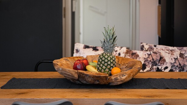 Un comedor con mesa de madera, frutero y lámparas colgantes.