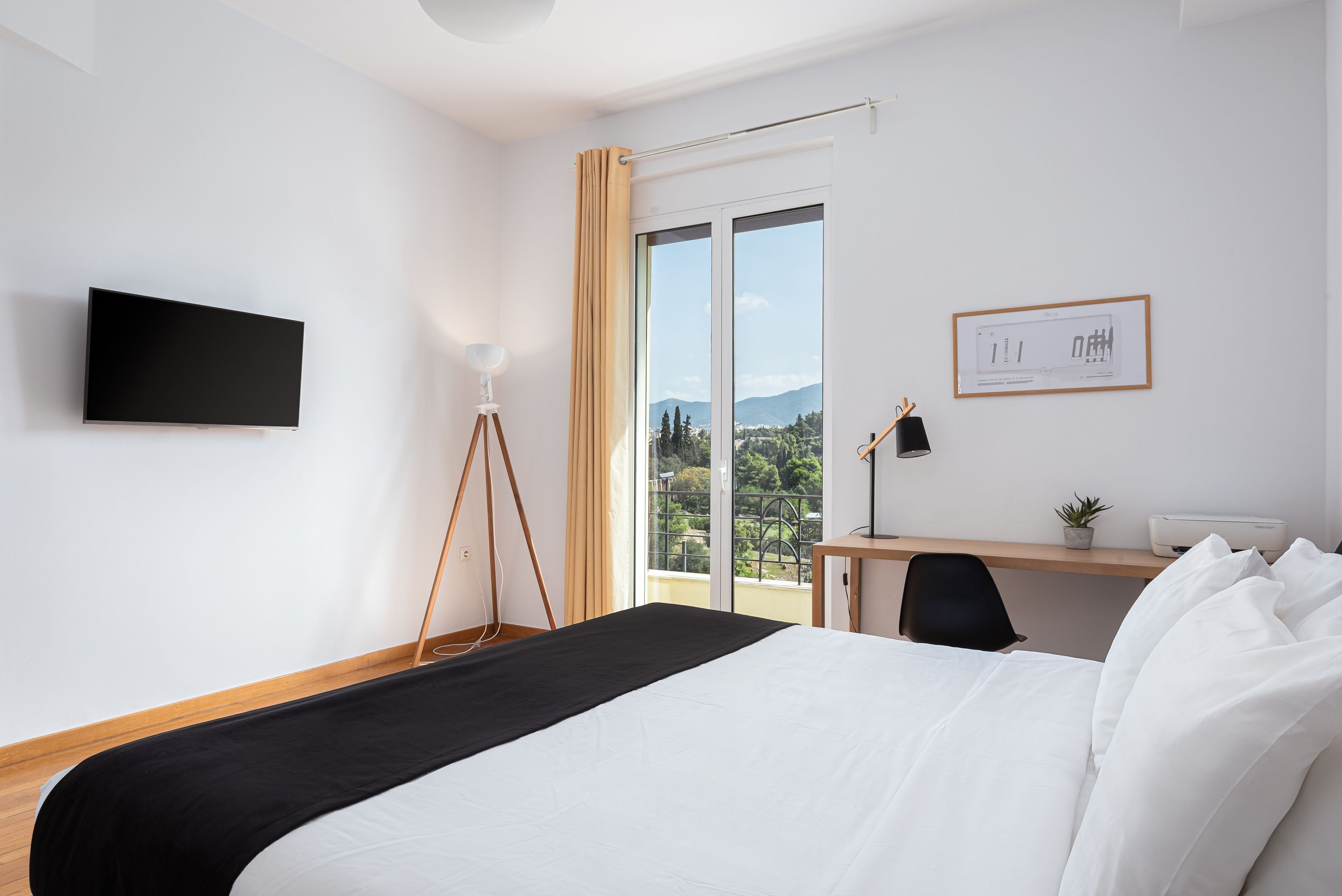 A hotel room with a bed, a desk, a chair, a TV, a lamp, and a window with a view of the outdoors.