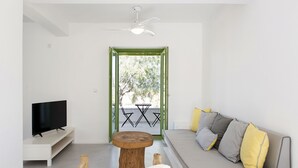A modern living room with a sofa, a TV on a stand, a round wooden table, and a balcony with a table and chairs.