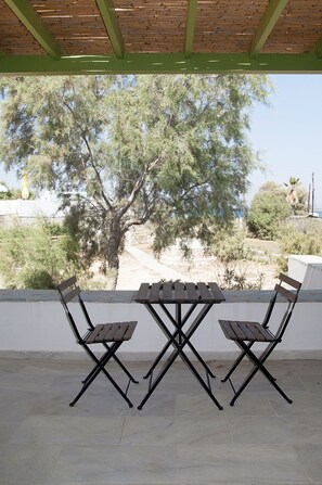 Un patio cubierto con dos mesas y sillas de madera, con vista a un árbol y el paisaje circundante.