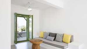 A modern living room with a wooden coffee table, a grey sofa with yellow and grey cushions, and a glass door leading to an outdoor area.