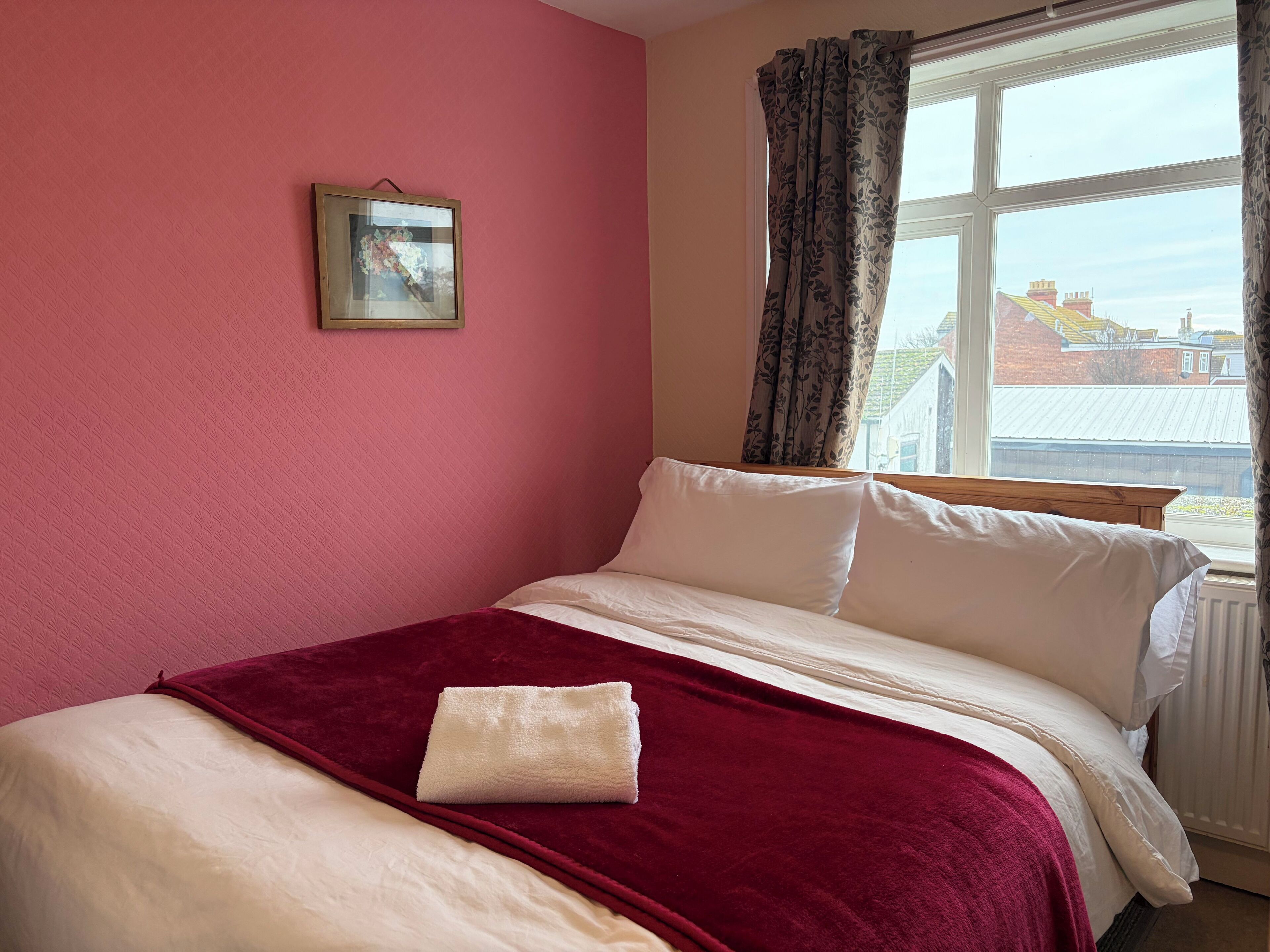Un dormitorio con cama, ventana con cortinas e imagen en la pared.