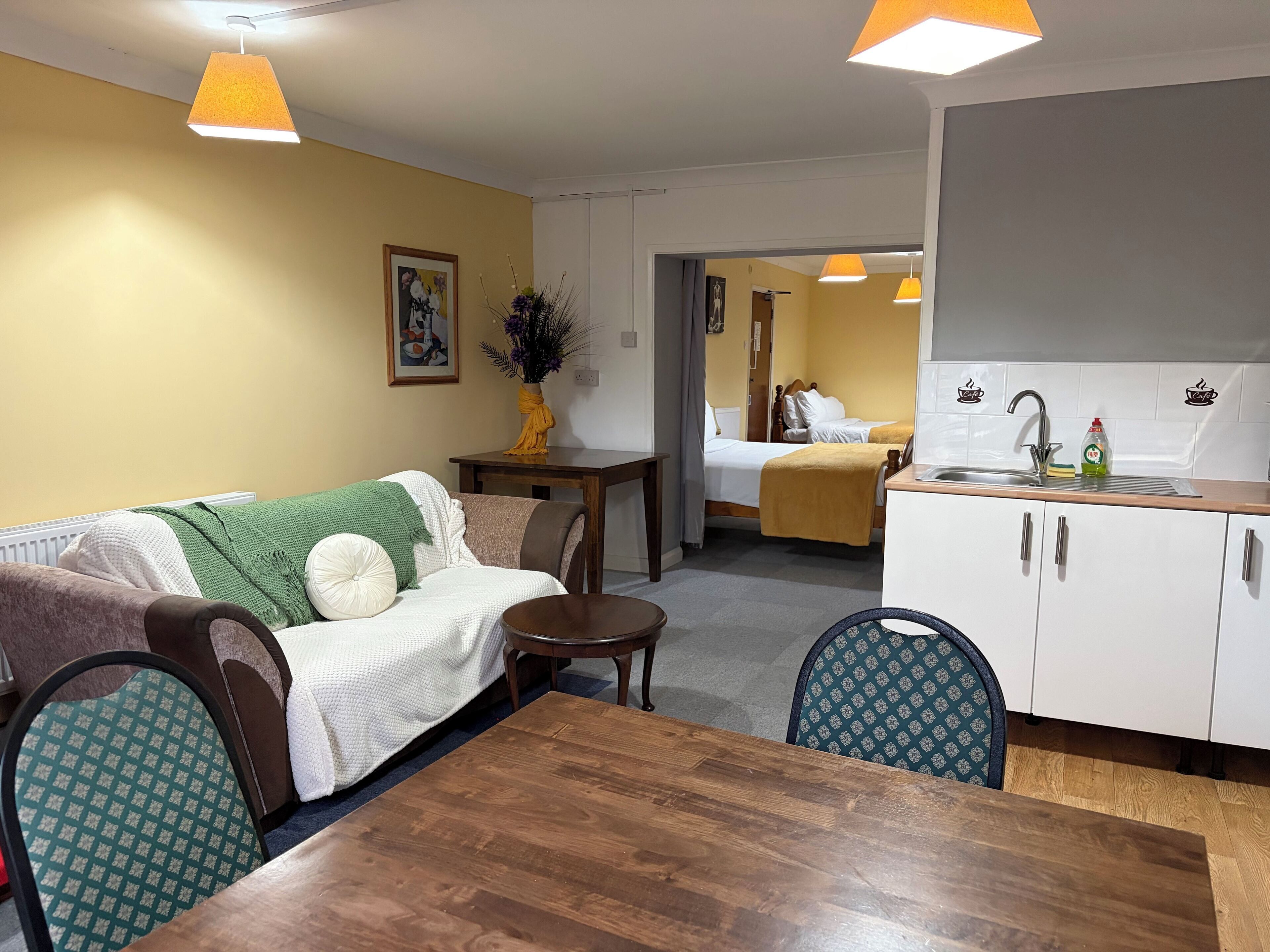 A compact living space with a dining area, kitchenette, and a bed in the background.