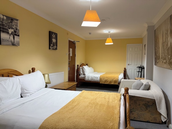 A hotel room with two single beds, a wooden headboard, a bedside table with a lamp, and a door leading to another room.