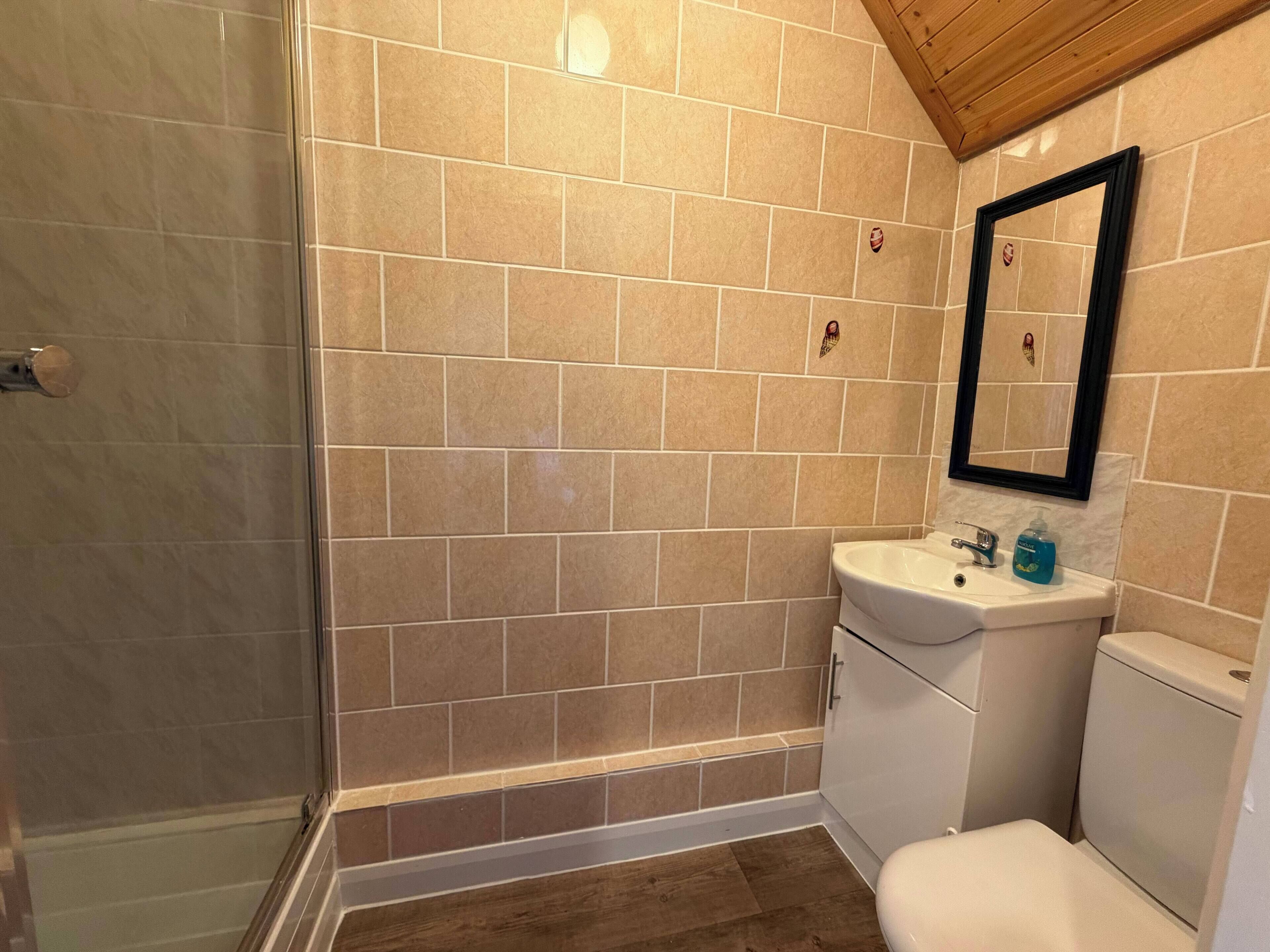 A bathroom with beige tiles, a white sink, a mirror, and a toilet.