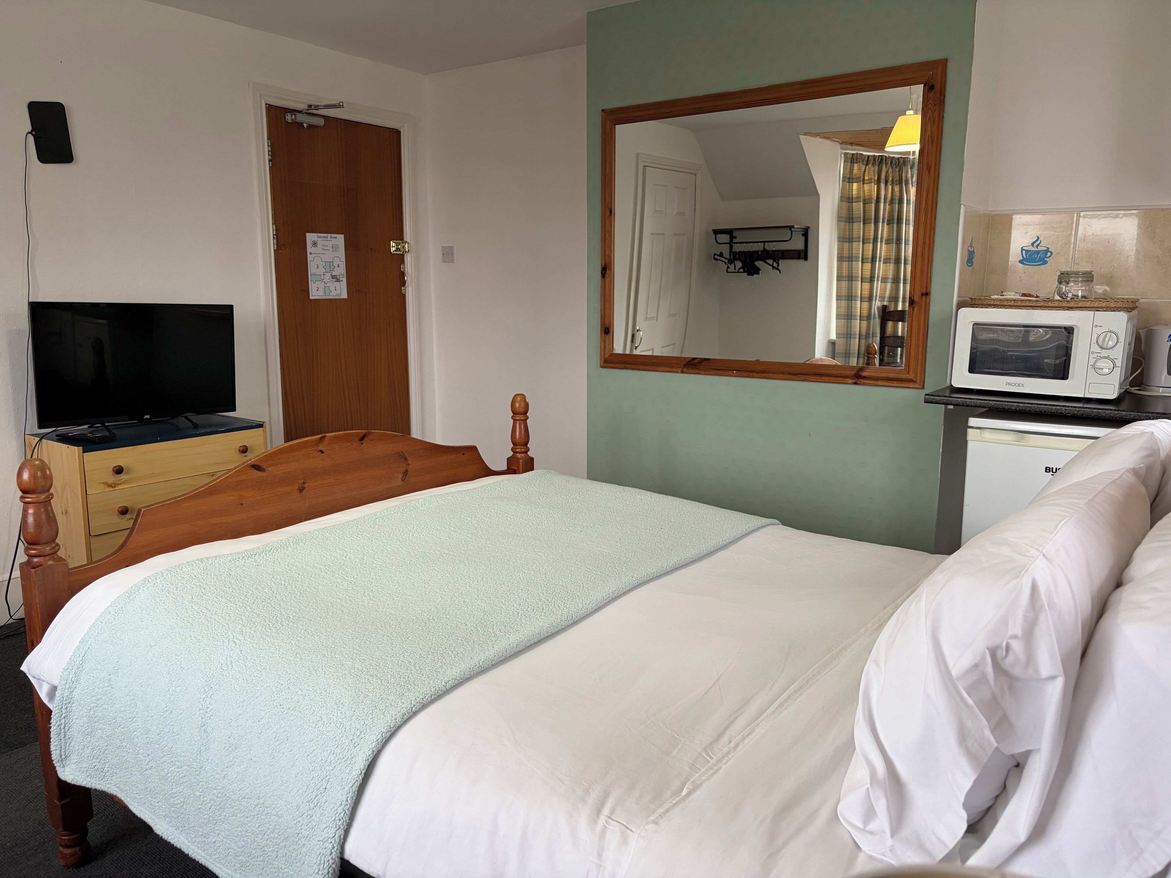 Ein Hotelzimmer mit einem Bett, einem Holzkoffer, einem Fernseher, einer Mikrowelle und einem Spiegel.