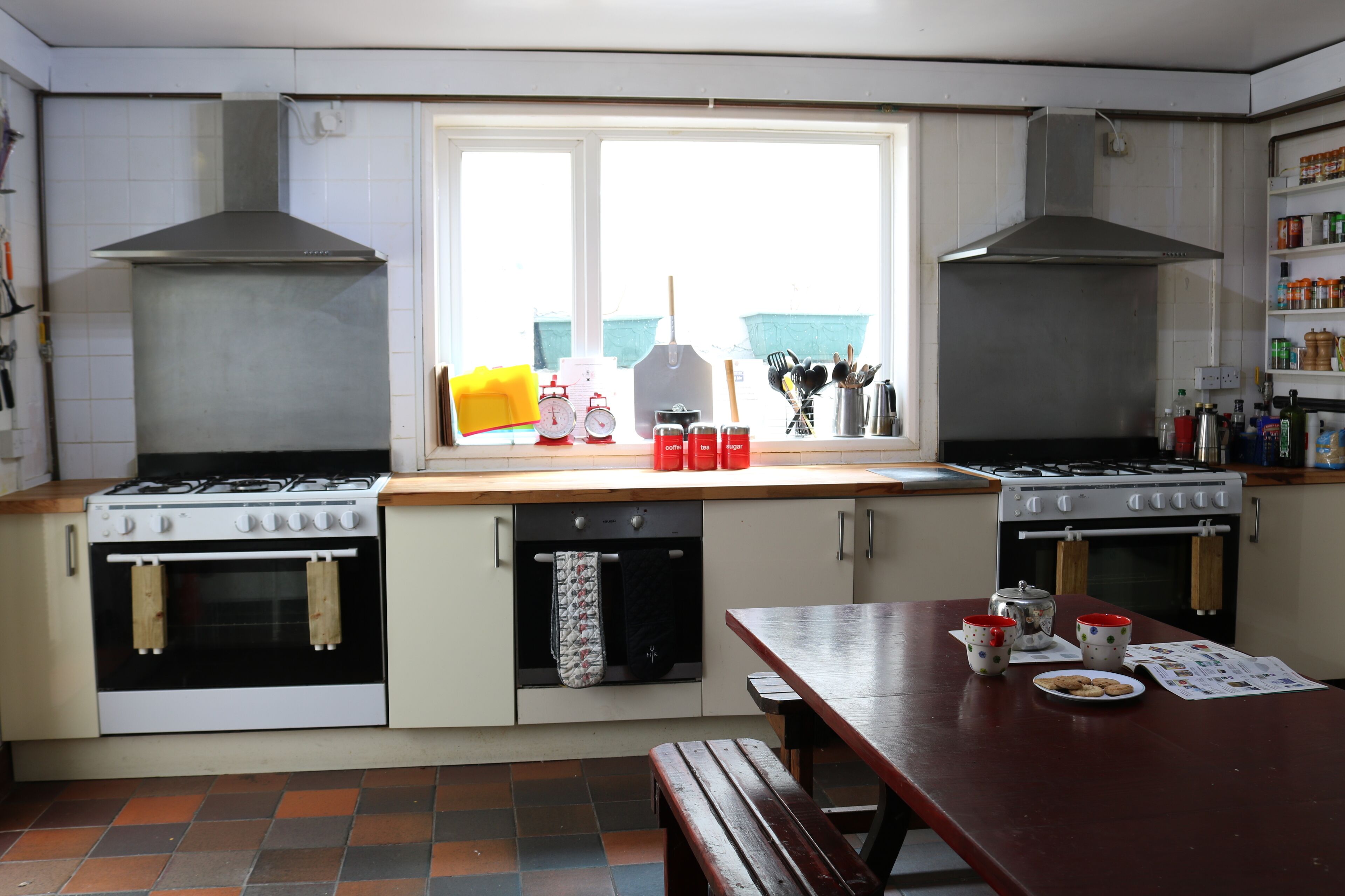 A kitchen with two stoves, a window, and a wooden table with a plate of cookies.