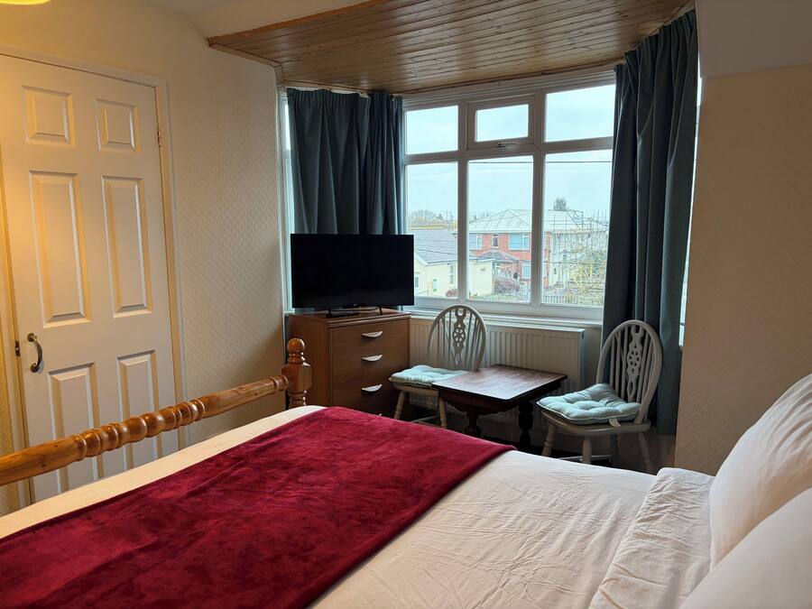 A hotel room with a bed, a desk, a chair, a television, and a window with curtains.