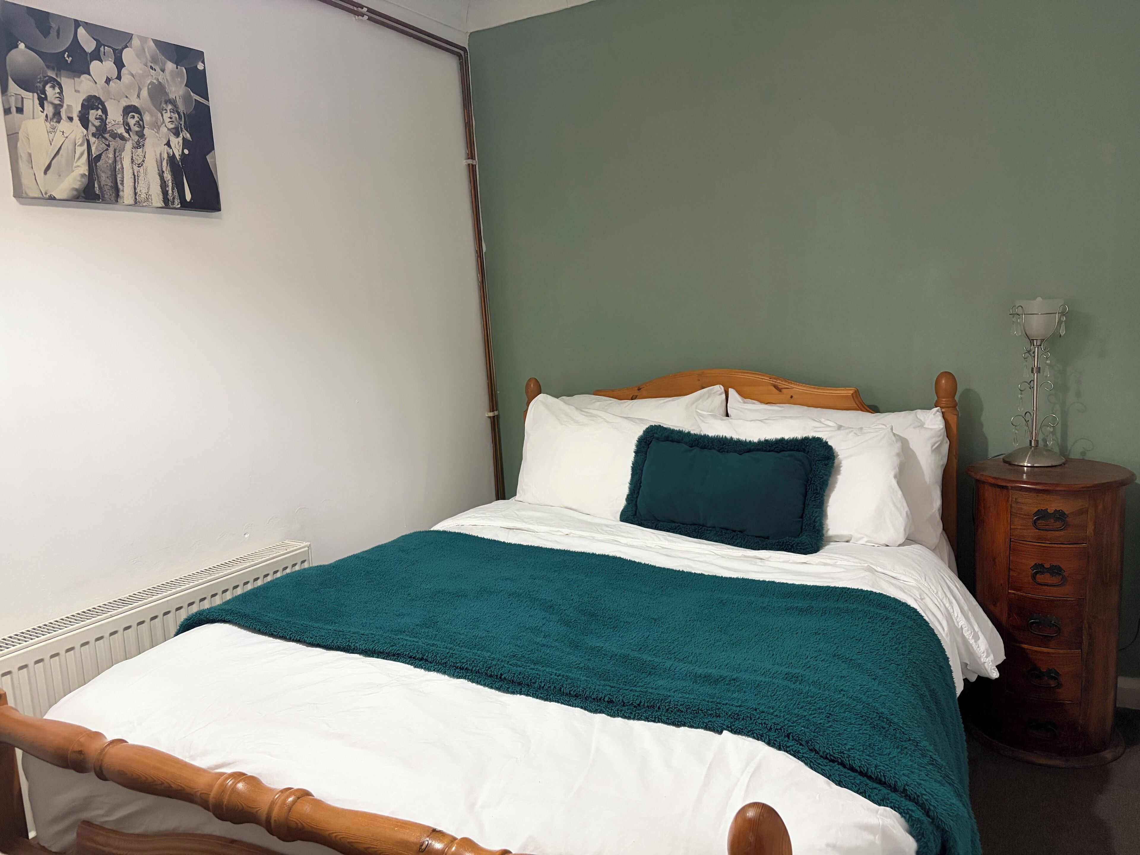 Una cama bien hecha con ropa de cama blanca y verde azulada, un cabecero de madera y una mesita de noche con una lámpara.